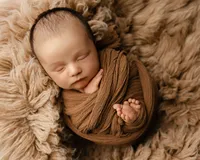Sleeping newborn baby wrapped in a warm brown swaddle and posed on a textured blanket during a studio session with newborn photographer Kaitlyn Dawn Photography.