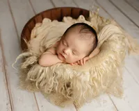 Sleeping newborn baby posed in a wooden bowl with a soft cream flokati blanket during a studio session with newborn photographer Kaitlyn Dawn Photography.