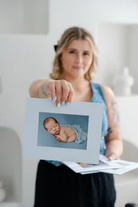 Woman holding a matted newborn portrait print with soft blue tones in a bright studio, Kaitlyn Dawn Photography, Yucaipa newborn photographer.