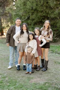 Family of six standing together in a grassy outdoor setting with coordinated earth-tone outfits, joyful candid moment captured by Kaitlyn Dawn Photography, professional family portrait photographer.