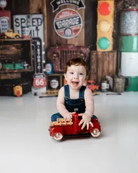 Birthday boy in overalls enjoying playtime in front of a classic car and Route 66-inspired cake smash backdrop.
Photograph by Yucaipa cake smash photographer Kaitlyn Dawn Photography.