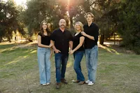 Family of four standing together in a grassy park during golden hour, coordinated casual outfits and warm sunlight captured by Kaitlyn Dawn Photography, professional outdoor family portrait photographer.