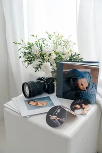 Professional photography setup with camera, newborn albums, and printed images styled with flowers in a bright studio, Kaitlyn Dawn Photography, Yucaipa newborn photographer.