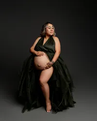 Artistic maternity photography portrait of pregnant woman seated wearing a dark green tulle maternity gown with dramatic lighting highlighting her baby bump by Inland Empire best maternity photographer Kaitlyn Dawn Photography.