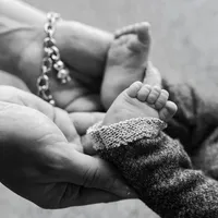 Black and white close-up of a newborn baby's tiny feet resting in a parent's hands during an intimate newborn photography moment captured by Kaitlyn Dawn Photography.