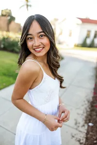Smiling high school senior girl posing outdoors in a white dress with soft sunset lighting, senior portrait by Kaitlyn Dawn Photography.