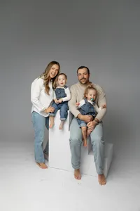 Mother standing beside father while holding their toddlers in a minimalist gray studio, candid family portrait by Kaitlyn Dawn Photography.