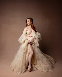 Elegant studio maternity portrait of a pregnant woman wearing a flowing neutral tulle gown against a warm brown backdrop photographed by Kaitlyn Dawn Photography.