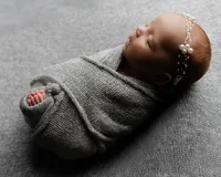 Sleeping newborn baby girl wrapped in a textured gray swaddle and wearing a pearl headband while posed on a soft neutral backdrop during a classic newborn photography session by Kaitlyn Dawn Photography.