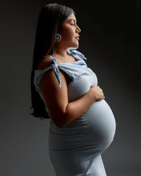 Pregnant woman in a light blue maternity dress posing in profile during a dramatic studio maternity portrait by Kaitlyn Dawn Photography.