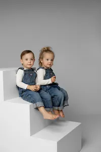 Two young siblings sitting side by side on white studio steps, coordinated denim outfits photographed by Kaitlyn Dawn Photography, sibling portrait photographer.