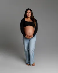 Expecting mom standing front-facing, gently holding her belly during a simple and modern maternity session by Kaitlyn Dawn Photography in the Inland Empire.