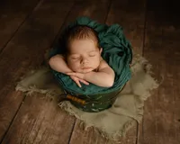 Sleeping newborn baby boy posed in a green bucket prop on a rustic wooden backdrop during a studio newborn photography session by Kaitlyn Dawn Photography.
