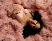 Expecting mother lying in a soft pink tulle maternity gown with hands on her belly during a studio maternity photoshoot by Kaitlyn Dawn Photography.