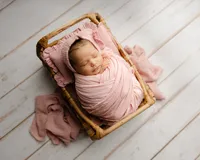 Sleeping newborn baby girl wrapped in a blush pink swaddle and posed in a wooden crate prop during a studio session with newborn photographer Kaitlyn Dawn Photography.