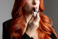 Close-up of woman with long red hair applying lipstick, photographed in studio. Photograph by Yucaipa branding photographer Kaitlyn Dawn Photography.