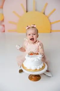 Baby in peach “one” dress crying during cake smash session with sunrise and balloon backdrop. Photograph by Yucaipa cake smash photographer Kaitlyn Dawn Photography.