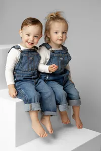 Two toddlers sitting together on white studio blocks in matching denim outfits, classic sibling portrait by Kaitlyn Dawn Photography, Inland Empire studio family photography.