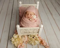Sleeping newborn baby girl wrapped in a soft pink swaddle and posed in a miniature white bed prop during a professional studio newborn photography session.