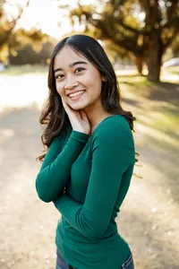 Close-up portrait of a smiling high school senior girl in a green top with warm sunset light, senior photography by Kaitlyn Dawn Photography.