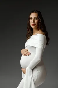 Pregnant woman in an elegant white gown smiling softly while cradling her baby bump during a maternity photoshoot in the Inland Empire by Kaitlyn Dawn Photography.