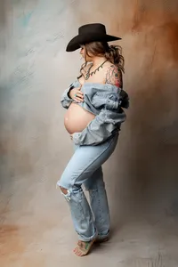 Pregnant woman wearing denim and a cowboy hat during a rustic styled studio maternity photography session by Kaitlyn Dawn Photography.