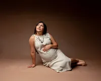 Pregnant mom reclining on the floor in a beige dress, softly cradling her belly during a maternity photoshoot in Yucaipa by Kaitlyn Dawn Photography.