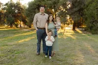 Parents standing with their two children in a grassy park at sunset, soft backlighting and relaxed smiles captured by Kaitlyn Dawn Photography, professional family photographer.