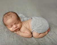Peacefully sleeping newborn baby posed on a neutral gray blanket wearing a soft gray wrap during a natural studio newborn photography session captured by Kaitlyn Dawn Photography.