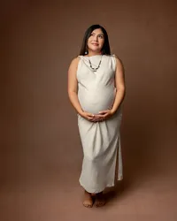 Expecting mom in a neutral beige dress standing against a warm backdrop, showcasing her pregnancy during an Inland Empire maternity session with Kaitlyn Dawn Photography.