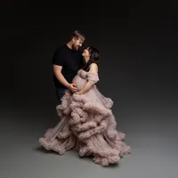 Romantic maternity studio portrait of expecting couple embracing with mother wearing a dramatic blush ruffled maternity gown and father gently holding her baby bump during maternity studio session by Kaitlyn Dawn Photography.