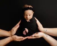 Sleeping newborn baby dressed in black while family hands gently surround the baby during a creative studio portrait by newborn photographer Kaitlyn Dawn Photography.