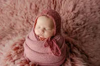 Sleeping newborn baby girl wrapped in a dusty rose swaddle and posed on a soft textured blanket during a studio session with newborn photographer Kaitlyn Dawn Photography.