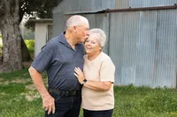 Elderly couple sharing a sweet candid moment outdoors near a rustic building, natural lifestyle portrait captured by Kaitlyn Dawn Photography, extended family photographer.