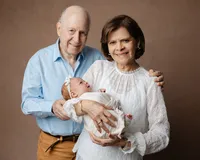 Grandparents smiling while holding their newborn grandchild wrapped in a soft neutral swaddle during a studio newborn family portrait by Kaitlyn Dawn Photography.