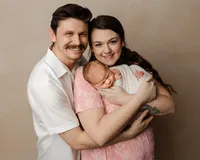 New parents embracing their sleeping newborn baby wrapped in a soft white swaddle during an intimate family newborn photography session by Kaitlyn Dawn Photography.