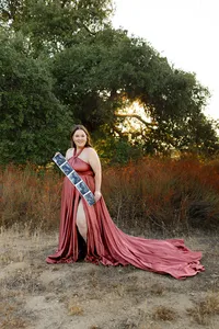 Pregnant woman wearing a flowing terracotta maternity gown standing outdoors at sunset holding ultrasound photos during a lifestyle maternity photography session captured by Kaitlyn Dawn Photography.