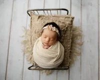 Sleeping newborn baby girl wrapped in a cream swaddle and posed in a vintage baby bed prop on a neutral wood backdrop during a newborn photography session by Kaitlyn Dawn Photography in Inland Empire.