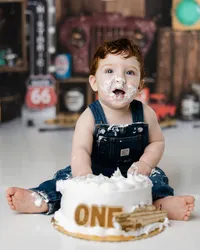 Little boy celebrating his first birthday with a cake smash, face covered in frosting and set against a retro garage theme.
Photograph by Yucaipa cake smash photographer Kaitlyn Dawn Photography.