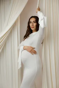 Pregnant mom posing in a white gown with one arm raised, softly cradling her baby bump during a maternity photoshoot by Kaitlyn Dawn Photography in Yucaipa.