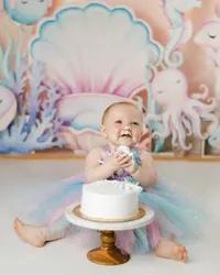 Baby enjoying a cake smash in a pastel mermaid-themed setup. Photograph by Yucaipa cake smash photographer Kaitlyn Dawn Photography.