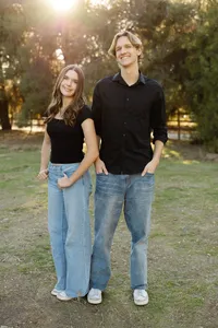 Siblings standing together in a sunlit park with coordinated black tops and jeans, modern outdoor portrait by Kaitlyn Dawn Photography, family and senior photographer.