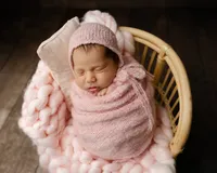 Newborn baby girl sleeping while wrapped in a soft pink swaddle and wearing a knitted bonnet while posed in a wicker basket with a fluffy pink blanket during a studio newborn photoshoot by Kaitlyn Dawn Photography.