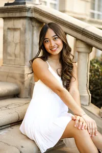 Close-up portrait of a smiling high school senior girl sitting on stone steps in a white dress, senior photographer Kaitlyn Dawn Photography.