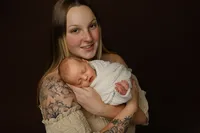 Mother smiling while holding her newborn during a studio session. Photographed by Inland Empire newborn photographer Kaitlyn Dawn Photography.