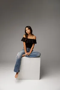 High school senior girl sitting on a white studio block wearing a black top and jeans studio senior photography by Kaitlyn Dawn Photography.