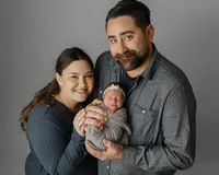 Parents smiling while holding their newborn baby wrapped in a soft gray swaddle during a studio newborn family portrait by Kaitlyn Dawn Photography.
