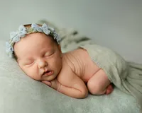 Sleeping newborn baby girl wearing a floral headband and posed on a soft green backdrop during a studio session with newborn photographer Kaitlyn Dawn Photography.