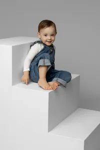 Smiling toddler girl sitting on modern white studio steps in a neutral gray setting, classic child portrait by Kaitlyn Dawn Photography, Yucaipa family photography studio.