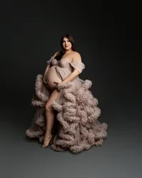 Pregnant woman posing in a dramatic blush ruffled maternity gown during an elegant studio maternity photography session highlighting her baby bump, photographed by Kaitlyn Dawn Photography.